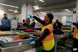 Un trabajador señala mientras la gente espera las pertenencias en el área de seguridad de la Administración de Seguridad del Transporte en el Aeropuerto Internacional Hartsfield-Jackson de Atlanta, el 25 de enero de 2023, en Atlanta, Georgia.