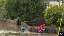 Un niño y un hombre andan en bicicleta a través de las inundaciones en Watsonville, California, el 11 de marzo de 2023.
