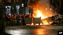 Los manifestantes se reúnen en una barricada con un coche de policía en llamas, no lejos del edificio del parlamento georgiano en Tbilisi, Georgia, el 9 de marzo de 2023.